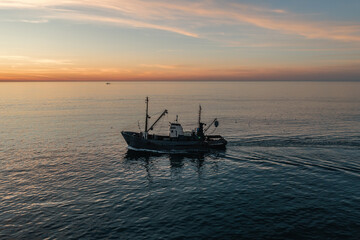 Fishing boat catching fish at sunset aerial view from drone. Small fishing trawler ship on sea surface.
