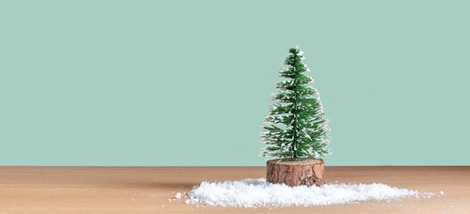 Small decorative snowy Christmas tree in front of green background.