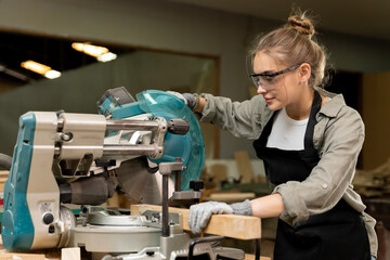 A female carpenter is working at a furniture factory with modern equipment and machinery.