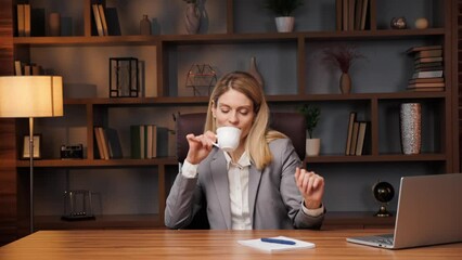 Funny happy businesswoman sitting at home office, working on laptop online, having fun, reading positive news, celebrating, dancing with joy, actively moving hands, drinking aromatic coffee.