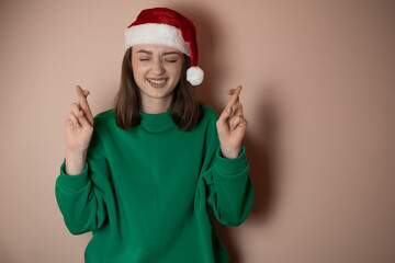 Merry young woman wear xmas sweater Santa hat posing do winner gesture celebrate clenching fists say yes isolated on plain pastel light green background Happy New Year 2023 celebration holiday concept