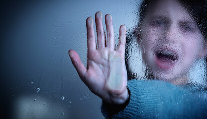 Protect children and young underage people from violence, exploitation, abuse, and neglect concept. Young girl showing stop gesture from behind wet glass. Copy space for design or text.