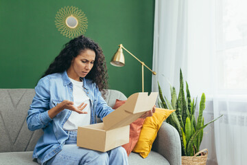 Dissatisfied woman buyer received wrong parcel and wrong product, cheated latina woman sitting on sofa at home in living room. - obrazy, fototapety, plakaty