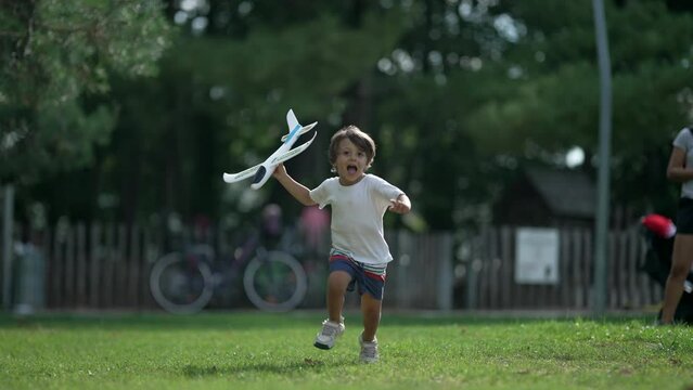 Young boy running with plane toy at park. Carefree Child throwing airplane glider outdoors having fun. Playful kid throws foam plane in sunny beautiful day