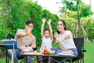 Young Asian parents doing activities eating and playing with their daughter in the front yard during the holidays happily.