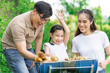 Young Asian parents doing activities eating and playing with their daughter in the front yard during the holidays happily.