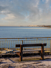 Wooden bench with stunning view on the ocean and town in the background. Blue cloudy sky. Galway city, Ireland. Nobody