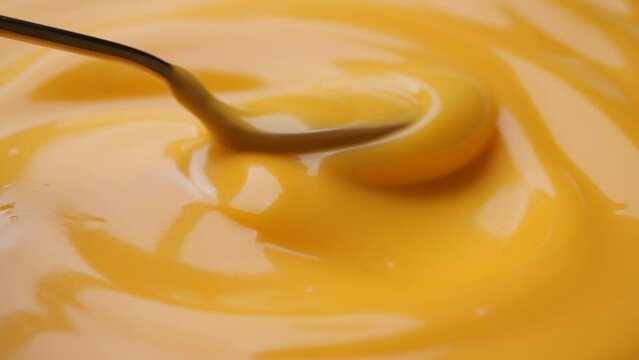 Stirring yellow cheese sauce with golden spoon