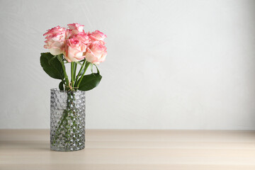 Vase with beautiful pink roses on wooden table. Space for text