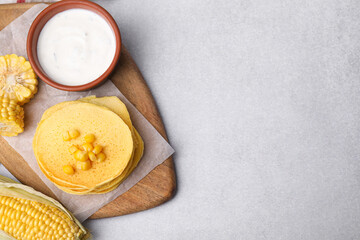 Tasty corn pancakes with sweet kernels and sauce served on light grey table, flat lay. Space for text