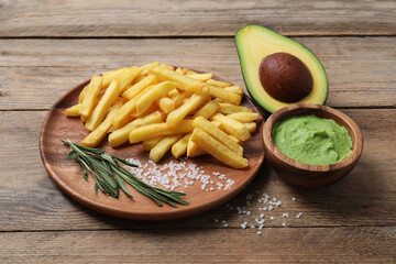 Plate with french fries, guacamole dip and avocado served on wooden table