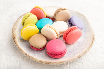 Different colors macaroons on ceramic plate on gray concrete background. side view, close up.