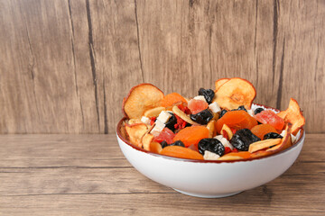 Bowl with different tasty dried fruits on wooden table. Space for text