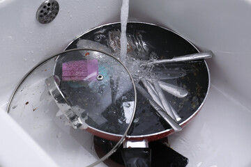Pouring water on dirty kitchenware and cutlery in sink