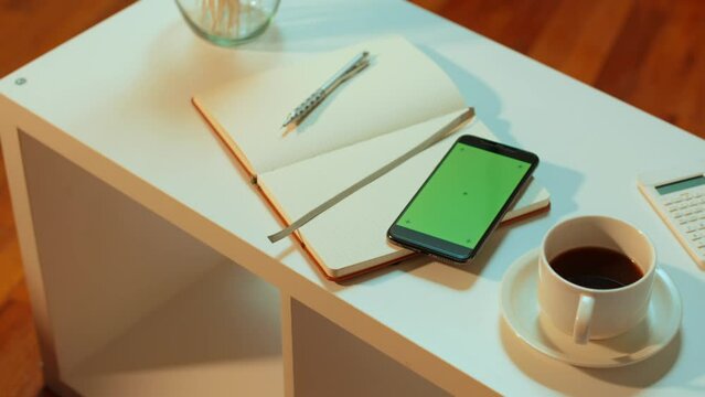 [Camera used: ARRI ALEXA, 50mm lens, slow motion] Slow pan of a green screen cell phone with tracking marks, placed on a coffee table at a coffee shop or living room setting.