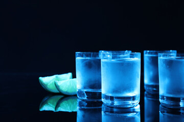 Shot glass of vodka with lime slices on dark background, space for text