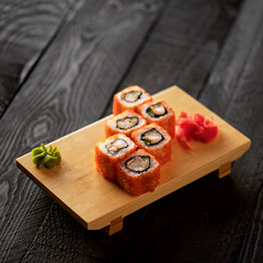 California rolls with caviar, avocado and shrimp.Japanese kitchen. Seafood dish. Vegetarian food. Set is served on wooden board with wasabi and ginger. Dark background. Soft focus. Copy space.