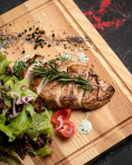 Grilled chicken fillet steak with salad of fresh vegetables and herbs on wooden board. Healthy food. Low calorie food. Dark background. Soft focus. Close-up. Top view.