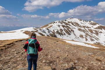 Obraz premium Woman with backpack on idyllic hiking trail with panoramic view of radar station on snow covered mountain peak Scharfes Eck seen from Zirbitzkogel, Seetal Alps, Styria (Steiermark), Austria, Europe