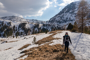 Fototapeta premium Woman walking on idyllic snow covered hiking trail to the snowcapped mountain peak of Zirbitzkogel, Seetal Alps, Styria (Steiermark), Austria, Europe. Landscape of hills, forest, pastures and ridges