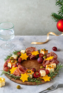 Christmas appetizers wreath on wooden board and grey background, Christmas tree branch, glass of water, forks. Vertical banner, copy space