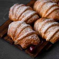 Puff pastry buns with cherries, sprinkled with powdered suga, on wooden boardr. Close-up, dark background. 