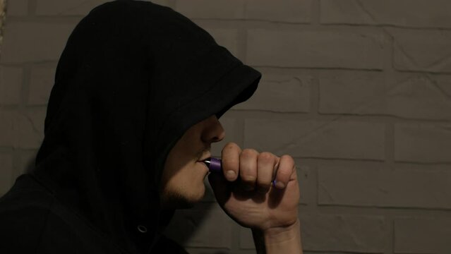 Young Man is smoking Vape Pod System at home near the gray wall. Electronic cigarette.