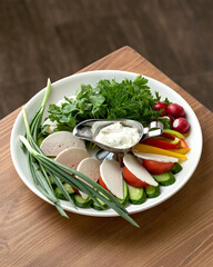 Mix of cheese, fresh vegetables and herbs, served with white sauce on white plate on wooden table. Healthy food. Vegetarian food. Low calorie meal. Close-up. Soft focus.