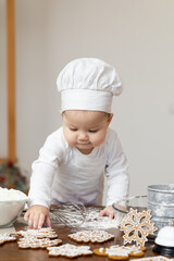 An Asian baby in a chef's cap and apron, smeared in flour, prepares Christmas ginger cookies