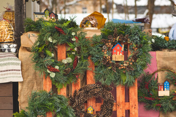 Beautiful handmade Christmas garlands or wreaths with wooden tiny house displayed at a street market in winter