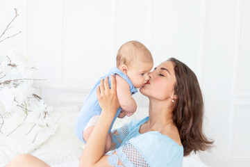 young mom with a newborn baby gently kisses him at home on the bed, the concept of a happy family and birth