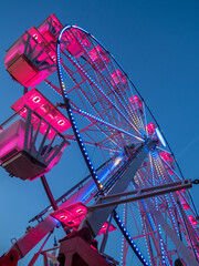 pink illuminated ferris wheel on a blue sky