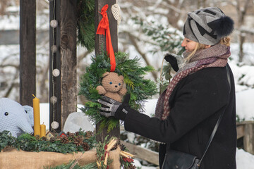 Beautiful girl in warm clothes buying a Christmas garland or wreath with teddy bear in a street market in winter