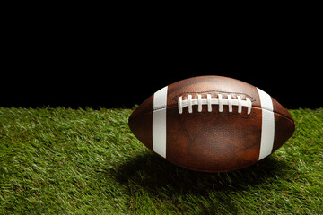 American football ball on green grass field background with space for text.
