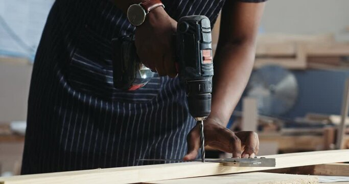 Close up of African Carpenter using electric power drill on a plank of wood