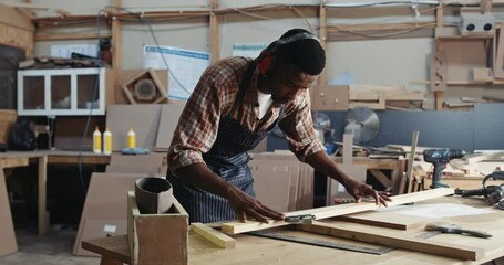 African male carpenter measuring up plank for wood working - Powered by Adobe