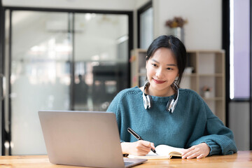 Young adult happy smiling Asian student wearing headphones talking on online chat meeting using...