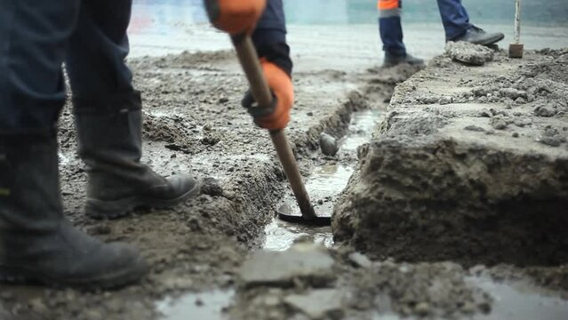 Worker shovels dirt from road. Preparation of foundation. Worker in mud. Hard work on construction site. 
