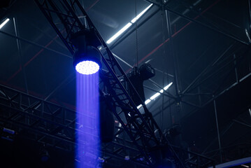 Moving head led wash on dark background. Light blue ray with smoke. Light truss and winch