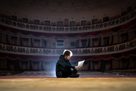 Professional male actor with a text in his hands on the stage of the theater against the backdrop of an empty hall