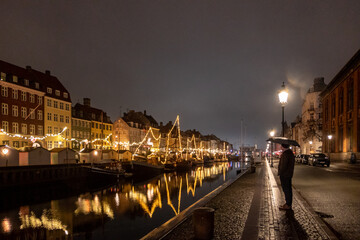 Fototapeta na wymiar Copenhagen, Denmark A single male tourist stands at the Nyhavn district at night.