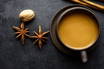 Masala tea in a clay mug and teapot. Traditional Indian hot drink with milk and spices on dark background
