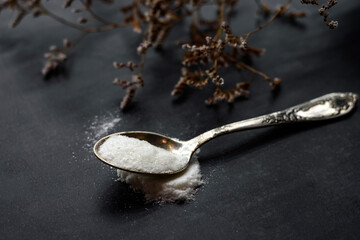 White vanilla powder in a spoon on a black background