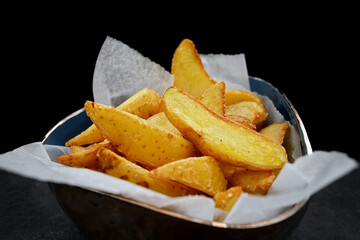 Fried potato wedges on paper, on a black