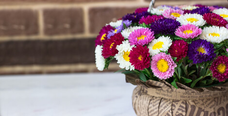 Bouquet of small chrysanthemums in the shape of a basket. Bouquet on a white table against a brick wall