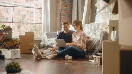 Moving in: Happy Young Homeowners: Couple Sitting on the Floor of their New Apartment Use Laptop Computer for Online Shopping. Planning Decoration of Sweet Home. e-Commerce, Buy, Purchase Concept