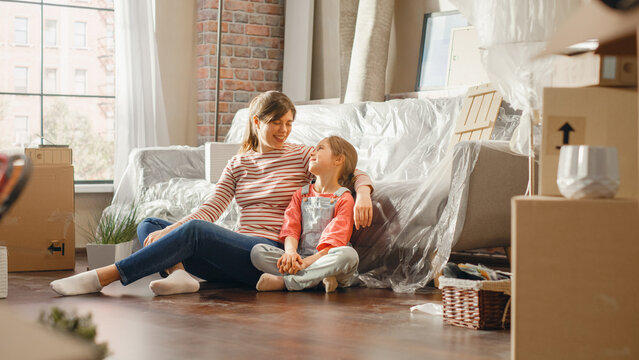 Moving Happy Mother and Daughter Talk, Sitting on a Living Room floor of their New Cozy Home. Cheerful Young Family, Dream, Imagine Good Times, Plan Apartment Decorations. Cardboard Boxes around.