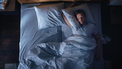 Top View Apartment Bedroom: Handsome Young Man Sleeping Cozily on a Bed in His Bedroom at Night. Comfortable Apartment with Guy Resting for Productive next Day. Top Down Above