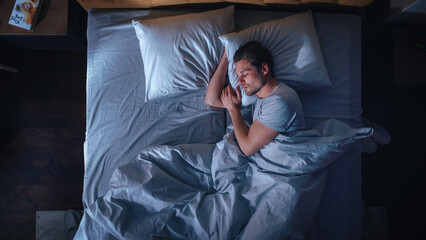 Top View Apartment Bedroom: Handsome Young Man Sleeping Cozily on a Bed in His Bedroom at Night....