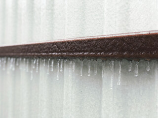 Heavy freezing rain in winter froze on a metal brown pipe and a white fence